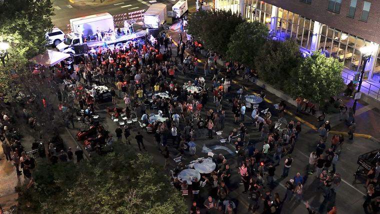 Crowd gathered around cocktail tables for live music on a closed street