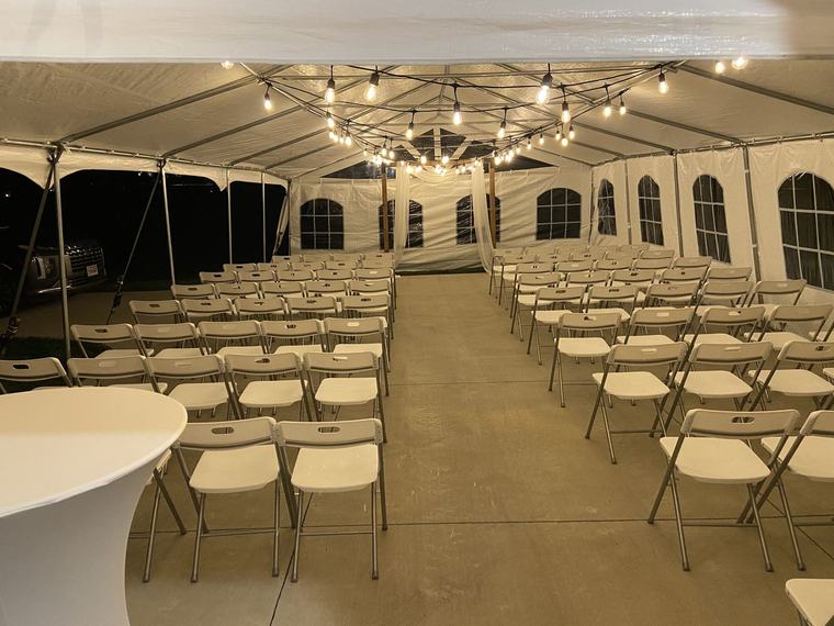 Rows of chairs set for a ceremony inside a tent strung with lights