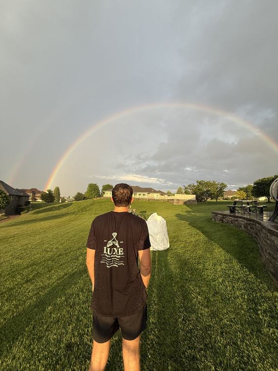 A Luxe crew member on the lawn under a rainbow after a setup