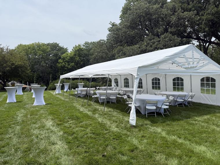 Long tent with cocktail tables running along a lawn