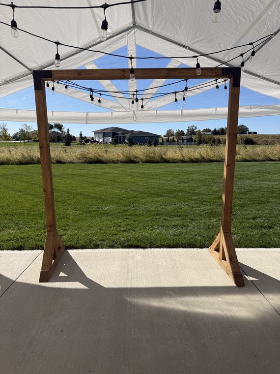 Wooden ceremony arch framed by a tent and string lights
