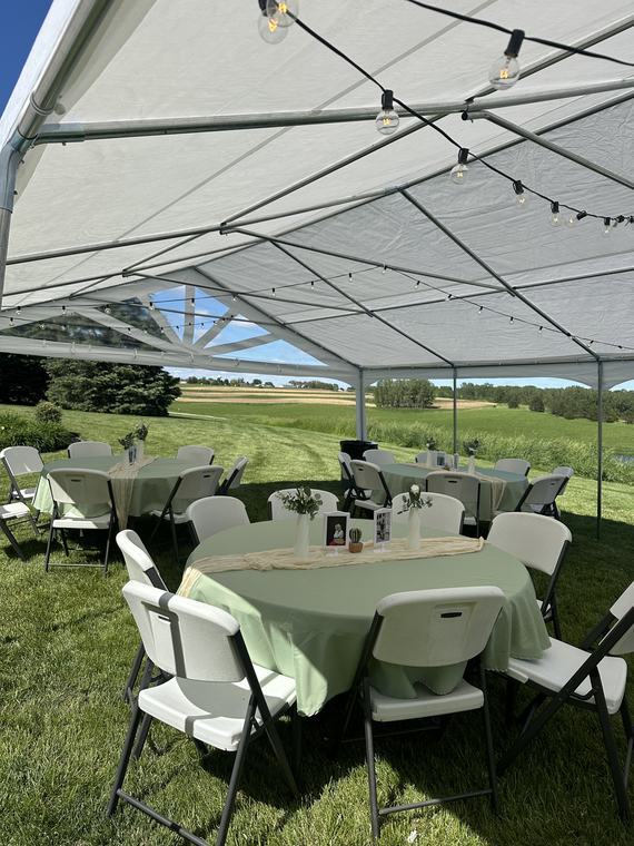 Round tables in sage linens under a tent, open farmland beyond